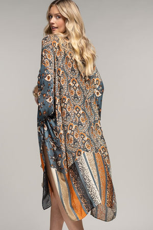 woman wearing a kimono in mix of botanical and geometric patterns,  open front with side slits in shades of deep teal blue, orange and beige, back view