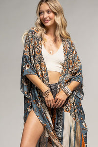 woman wearing a kimono in mix of botanical and geometric patterns,  open front with side slits in shades of deep teal blue, orange and beige