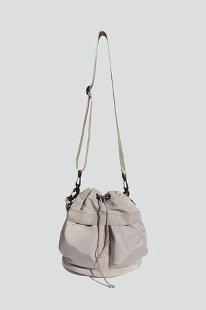 Sage nylon bucket bag with  drawstring closure, two detachable strap options (long strap, short handle) with exterior pockets in front.