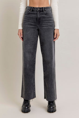 Person wearing black straight-leg jeans on a plain background, wide leg, full-length, raw edge hem