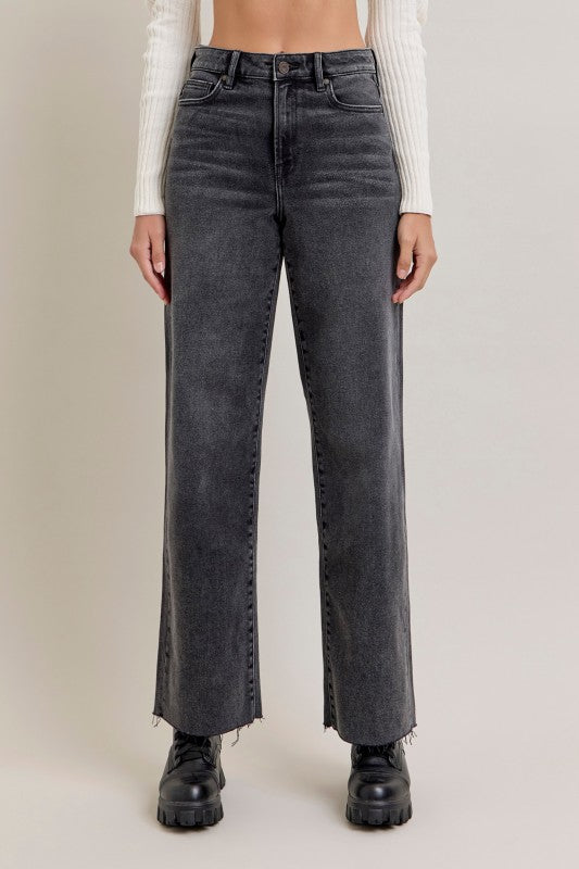 Person wearing black straight-leg jeans on a plain background, wide leg, full-length, raw edge hem