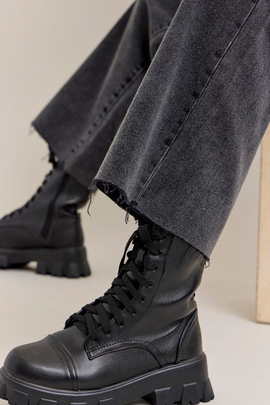 Black leather boots worn with gray pants on a neutral background, raw edge hem
