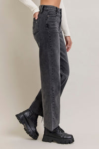 side view of Person wearing black high-waisted jeans and black boots on a plain background, wide leg, full-length, raw edge hem