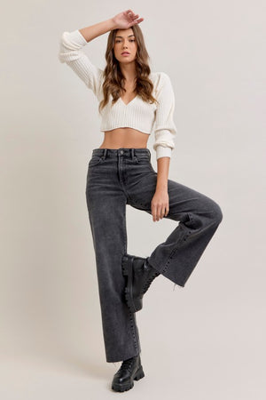 Woman wearing a white cropped sweater and black high-waisted jeans on a plain background, pants are wide leg, full length with raw edge hem