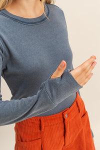 close up of woman wearing mineral washed blue t-shirt with thumb hole long sleeves and reversed stitching around collar and shoulders, exposed seam down the back