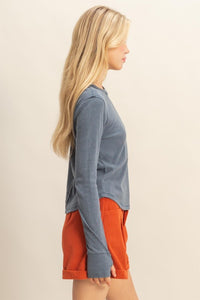 side view of woman wearing mineral washed blue t-shirt with thumb hole long sleeves and reversed stitching around collar and shoulders, exposed seam down the back