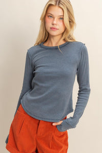 woman wearing mineral washed blue t-shirt with thumb hole long sleeves and reversed stitching around collar and shoulders, exposed seam down the back