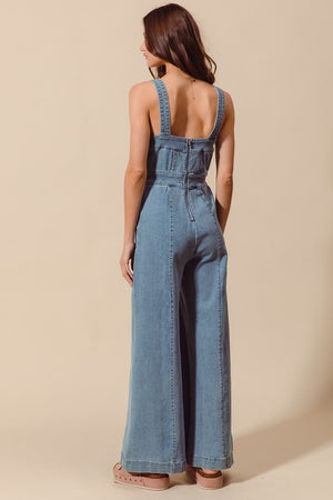 Sleeveless medium wash denim jumpsuit with pockets, back zipper closure, and wide legs