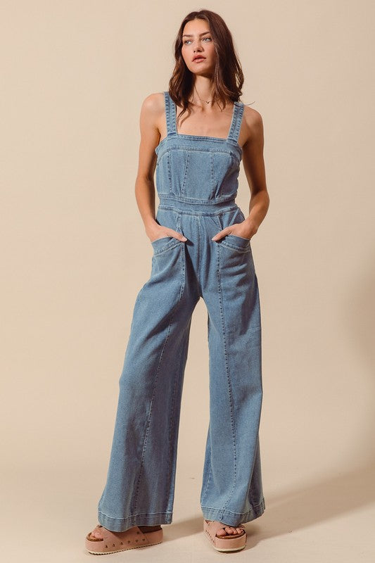 Sleeveless medium wash denim jumpsuit with pockets, back zipper closure, and wide legs