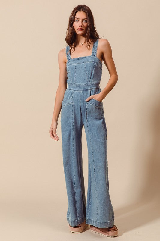 Sleeveless medium wash denim jumpsuit with pockets, back zipper closure, and wide legs