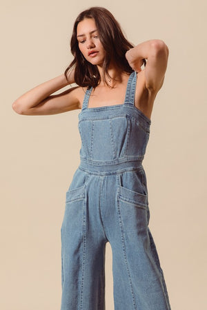 Sleeveless medium wash denim jumpsuit with pockets, back zipper closure, and wide legs