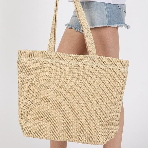 Beige woven tote bag held by a person wearing denim shorts on a white background