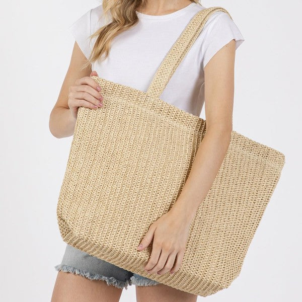 Person holding a woven beige tote bag against a plain background