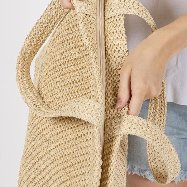 Close-up of a beige woven bag held by a person with a neutral background
