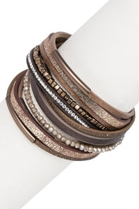 Stack of brown leather bracelets with metallic accents on a white surface