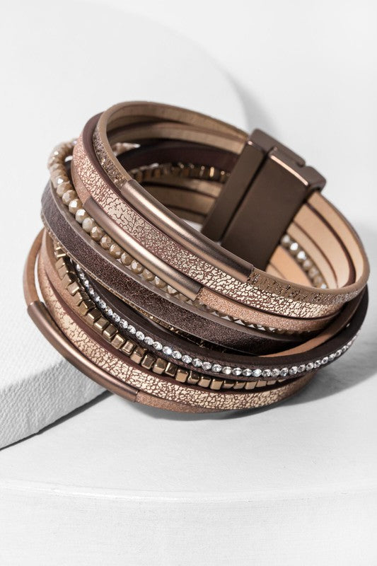 Stack of brown leather bracelets with metallic accents on a white surface